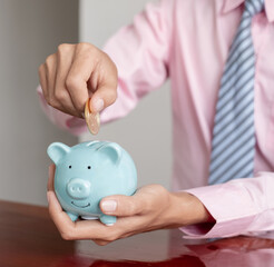 The hand of a businessman puts coins in a piggy bank, saves money with coins, steps into a...