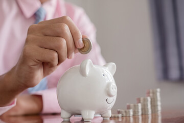 The hand of a businessman puts coins in a piggy bank, saves money with coins, steps into a...