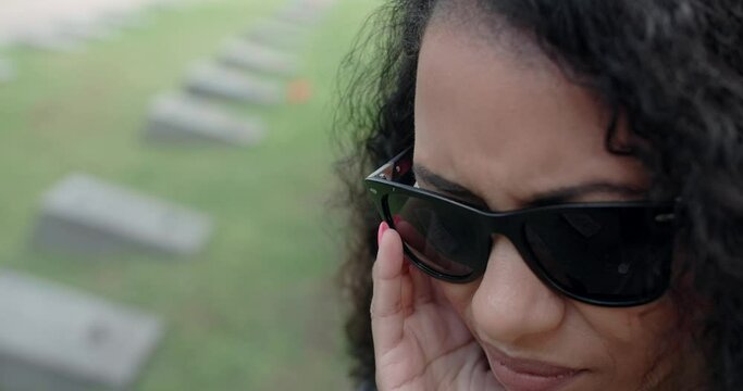 Portrait of the sorrowing black woman in sunglasses standing on the cemetery. Funeral and farewell, honoring the passed relatives. 4k 60p Prores