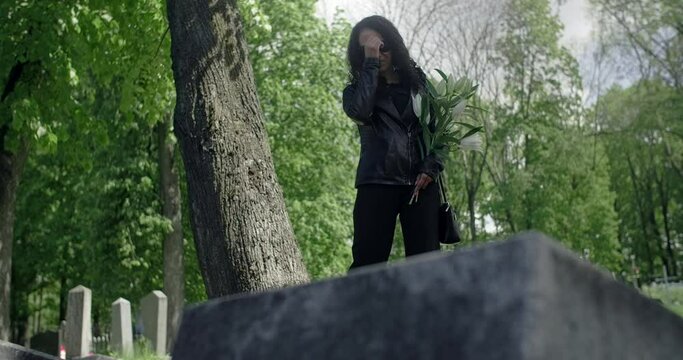Portrait of the sorrowing black woman in sunglasses standing with flower at the cemetery. Funeral and farewell, honoring the passed relatives. 4k 60p Prores