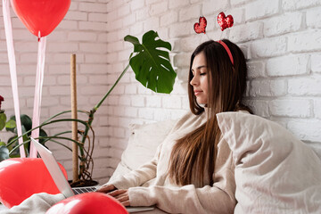 Young beautiful woman sitting in the bed celebrating valentine day working on laptop
