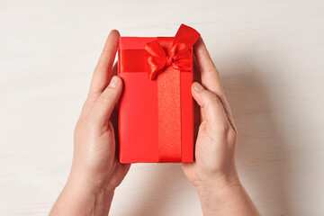 Female hands holding a bright red gift with a ribbon. Top view. Presenting a gift