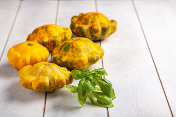 Yellow patissons or squash and a basil leaf on a light wooden background