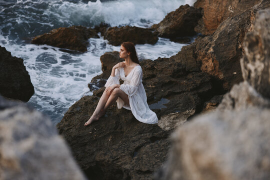 pretty woman with wet hair in white dress sits on waves stones unaltered