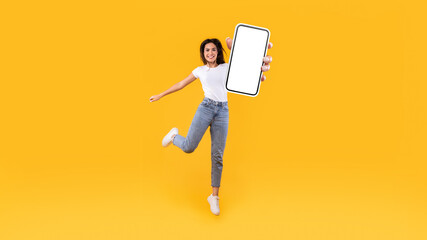 Happy woman showing white empty smartphone screen and jumping