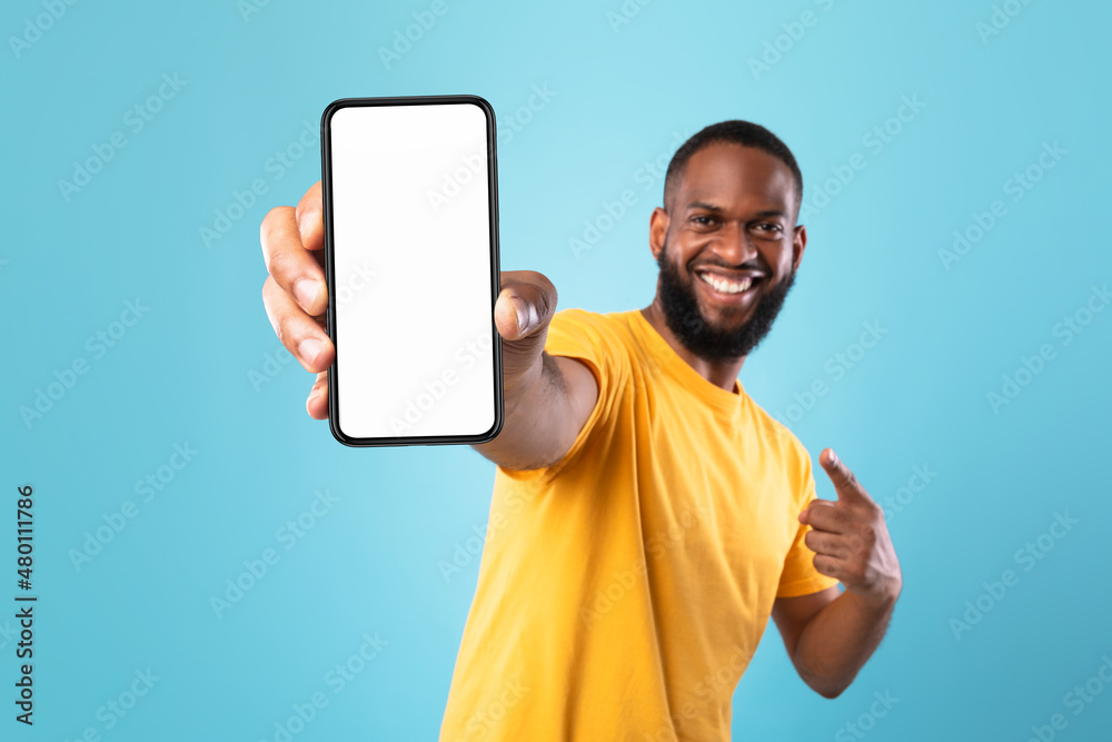 Aufkleber excited black guy pointing at cellphone with empty screen on blue background, mockup for website or 