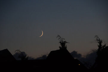 The New Moon seen at dusk over the silhouettes of a settlement.