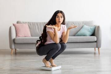 Surprised Indian lady sitting on scales, cannot understand lack of weight loss at home, copy space