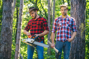 Woodcutters with chainsaw lumberjacks with axe. Hipsters men on serious face with axe. Lumberjack brutal and bearded holds axe. Two lumberjacks in forest