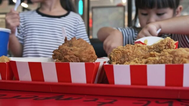 Cute little Asian girl eating fried chicken and french fries together at a fast food restaurant.