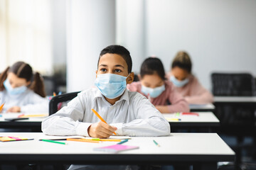 Girl in mask sitting at desk writing in classroom