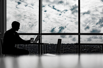 silhouette of a businessman working in an office with large windows.
