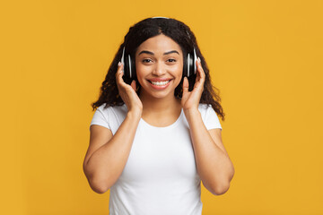 Fototapeta premium Excited african american lady in wireless headset listening to music, enjoying good sound over yellow background