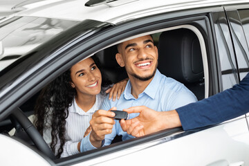 Happy middle-eastern couple sitting in car in huge showroom