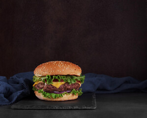 Juicy delicious burger with salad and onions on slate plate, blue napkin