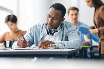 Black male student sitting at desk in classroom writing exam