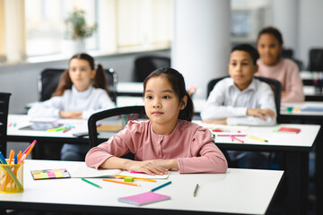 Portrait of focused asian girl sitting at desk in classroom