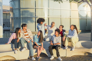 Big group of happy teenage friends talking in a bench in the street of the student campus.