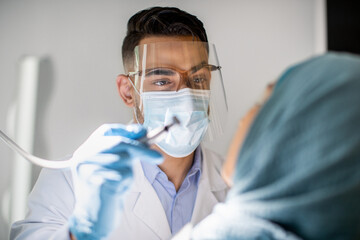 Fototapeta na wymiar Arab Dentist Doctor In Medical Mask And Face Shield Checking Patient's Teeth