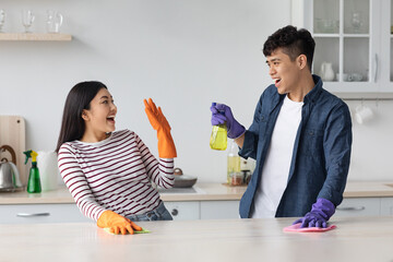 Joyful asian lovers having fun while cleaning kitchen together