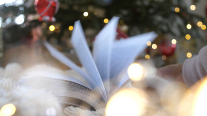 Christmas book mystically turns pages against background of Christmas decorations with tree garlands, balls and bokeh lights. Christmas, New Year. Christmas miracle, mysticism.