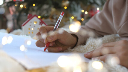 Close up hands of female writing letter and wish list at Christmas Eve. Girl writing in notebook. Woman hand holding pen on notepad at home on winter holidays xmas.