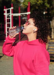 curly hair woman with a headphones drinking water on the playground