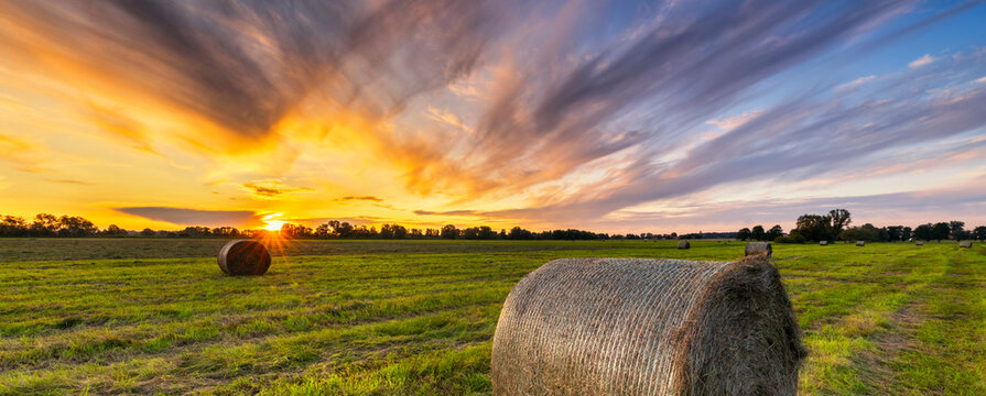 Beautiful sunset over green meadow with hay bales