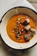 pumpkin cream soup in a handmade ceramic bowl. creamy pumpkin soup with croutons, cream and pumpkin seeds. serving creamy pumpkin soup on a marble table.seasonal hot dish