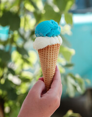 Hand holding waffle cone with two ice cream balls on the street Refreshing snack on a hot day Vertical photo