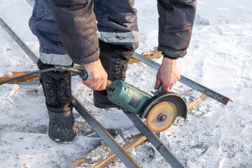 A worker cuts a metal bar with a circular saw in winter. Close up photo of a man holding a circular...