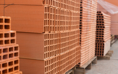 Red brick packed in stacks are stored on ground outdoors at a hardware store warehouse
