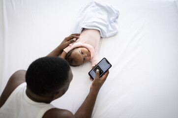 Father using cell phone and raising a baby on the bed at home.