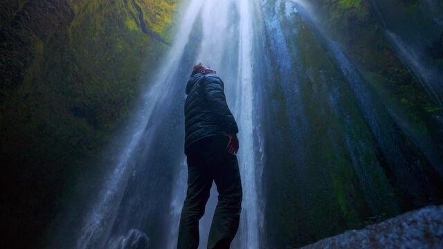 Male Tourist Standing On Rock Against Plummeting Waterfall In Gljufrabui, Iceland. low angle