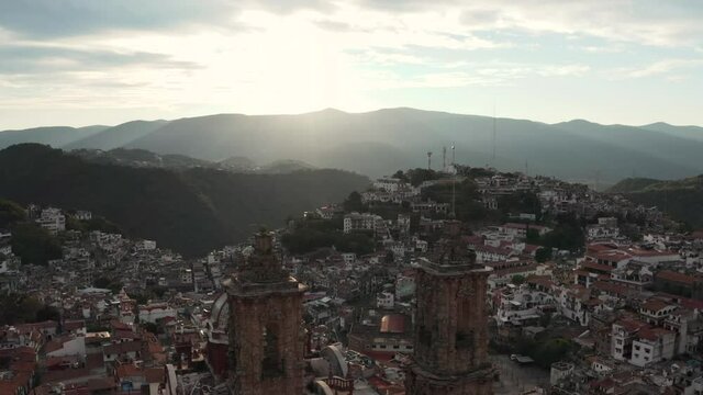 Flying above Church of Santa Prisca de Taxco with sunset sunlight as backlight, drone aerial view of landmark and cityscape
