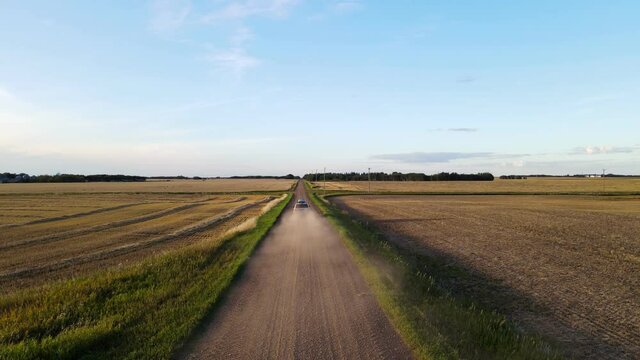 Drone Hovering Low Above A Red Dirt Road In Rural Countryside Setting. Then Silver Car Is Driving Fast Underneath The Drone And Headed Off Into The Distance Whirling Up Lots Of Dust.