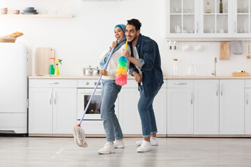 Joyful muslim couple cleaning floor and having fun in kitchen