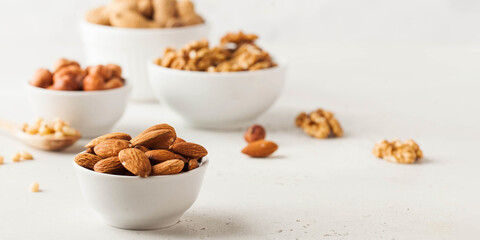 Almonds and other nuts in white bowls on a white background. Banner