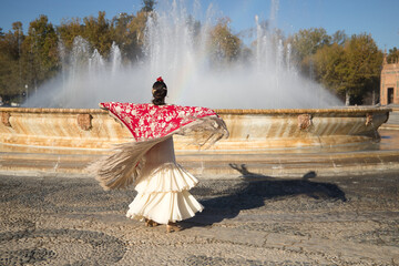 Young flamenco woman, Hispanic and brunette, with typical flamenco dance suit, dancing with red...