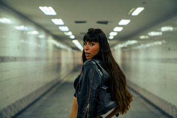 Obraz premium Portrait of Fashionable Hispanic woman in stylish clothing walking down cross street tunnel in the city at night. Confidence female in leather jacket enjoy urban outdoor lifestyle nightlife in summer