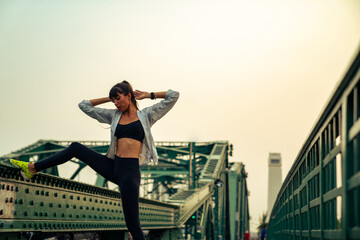 Fototapeta na wymiar Confidence Hispanic woman in sportswear stretching leg while jogging in the city at summer sunset. Healthy wellness female athlete enjoy outdoor lifestyle sport training workout running exercise
