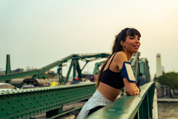 Hispanic woman listening to music from earphones and smartphone application while jogging in the city at summer sunset. Healthy female athlete enjoy outdoor sport training workout exercise and running