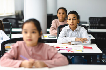 Portrait of focused small boy sitting at desk in classroom