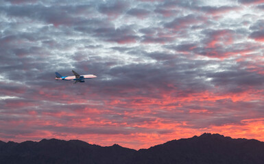 Fototapeta na wymiar International airplane in the sky above mountains during dramatic sunrise