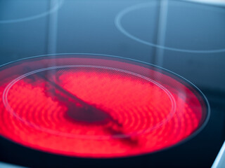 Close-up of kitchen stove with ceramic hob turned on and glowing red. 