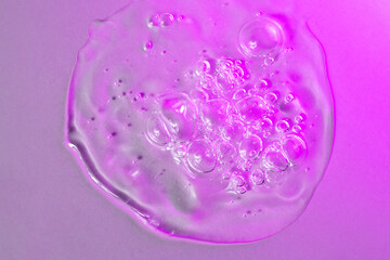Facial serum drop with bubbles in bright pink neon light macro. Liquid bubbly gel with hyaluronic...