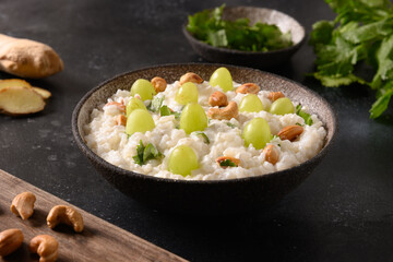 Curd Rice with cashews, grapes, cilantro, ginger on a dark background. Indian South cuisine. Close up.
