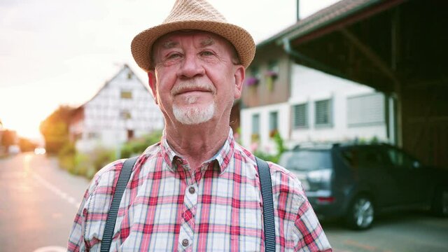 Portrait of bearded middle-aged man looking at camera standing in the street. Agricultural worker standing in front of big tractor in agricultural farm.