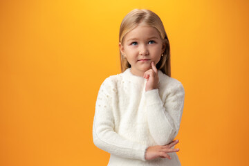 Little girl thinking and looking up over yellow background