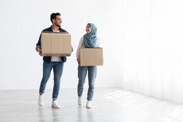 Smiling muslim couple moving to new apartment, full length photo